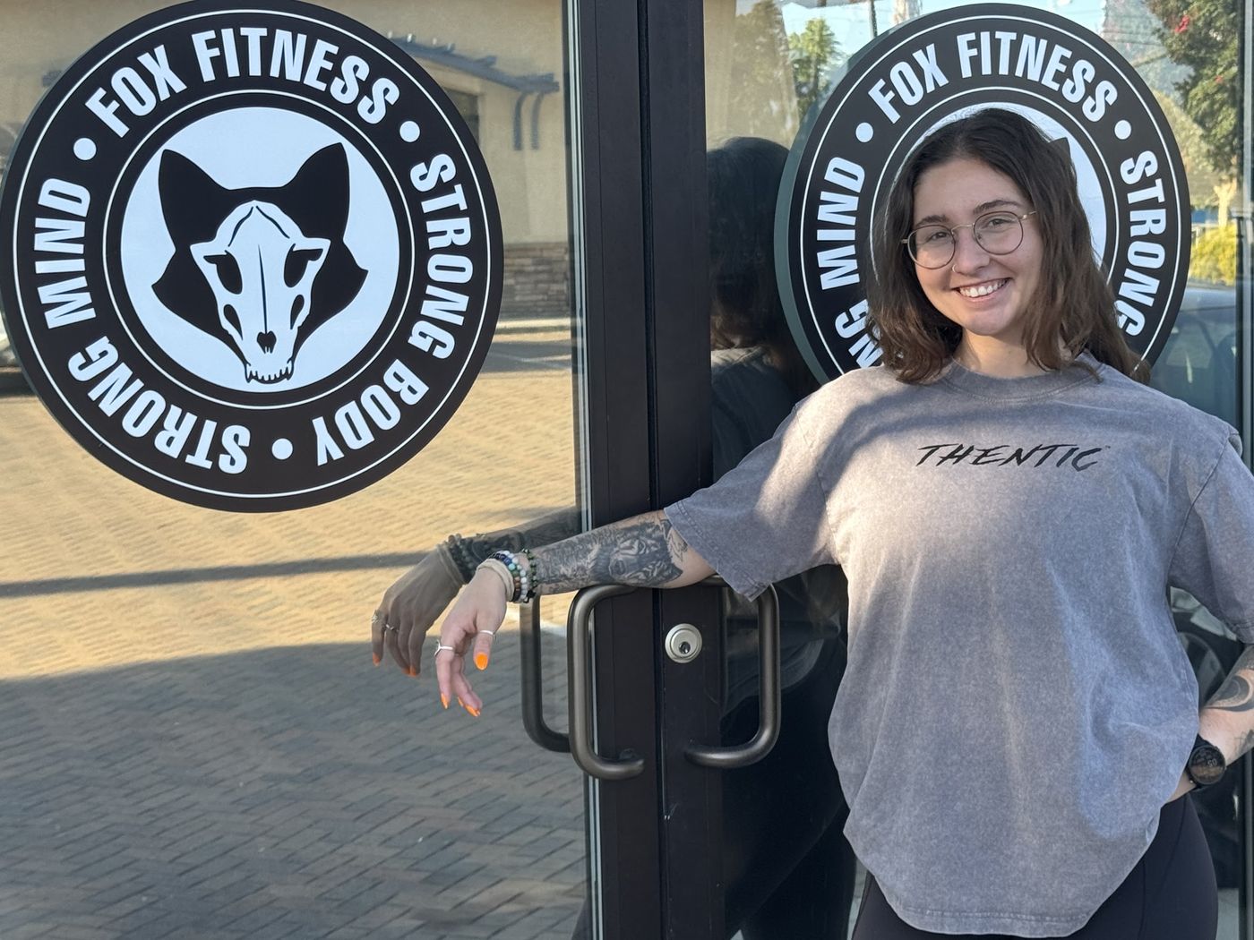 Dr. Robin Fox, owner of Fox Fitness, smiling at the gym’s front door beside the Fox Fitness logo